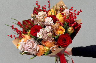Christmas bouquet with red roses, peach garden roses, blush lisianthus, red berries, and festive greenery, arranged in a premium holiday floral wrap