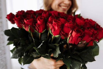 Woman holding a large bouquet of long-stem red roses, the rose color that means romantic love