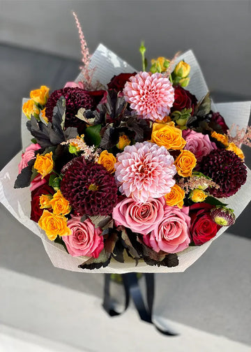 Dahlia and rose bouquet in fall colors, wrapped in paper with a ribbon, seen from above on a concrete ledge