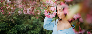 Woman in a light blue dress standing among cherry blossom trees with pink flowers.
