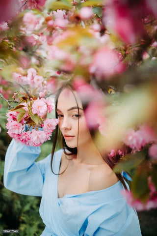 Woman in a light blue dress holding pink flowers amidst cherry blossoms