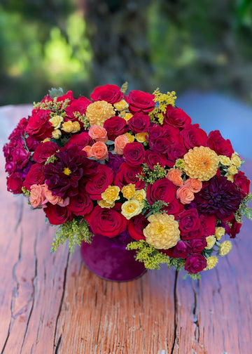 Fall roses and dahlias box in burgundy velvet with red roses, orange dahlias, purple carnations and warm spray roses on a wooden table