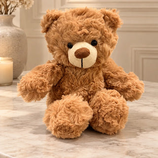 Plush teddy bear with a fluffy caramel coat and cream muzzle sitting on a marble table, front view