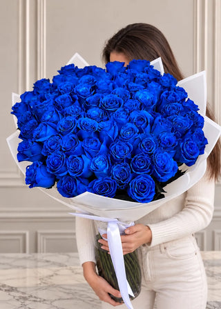 Large blue roses bouquet in paper wrap with a long ribbon, standing in a tall glass vase held in both hands
