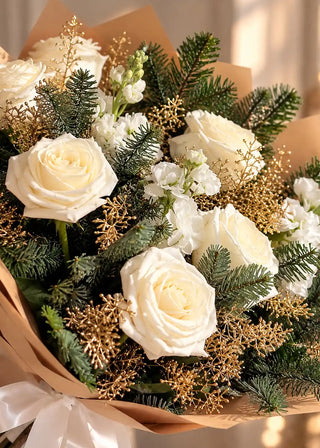 Close view of ivory roses and white stock among fir branches and gold-painted sprigs in a white Christmas bouquet