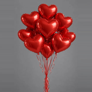 Bunch of red foil heart helium balloons on curled red ribbons, against a plain gray background