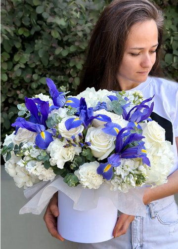 Iris and rose bouquet in a round white box with white hydrangea and carnations, held in both hands outdoors