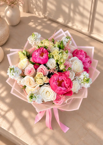 Pink peony bouquet with coral peonies, pink and white roses, white stock and astilbe in paper wrap, top view