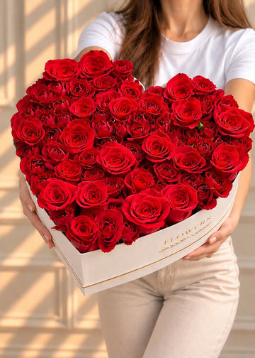 Heart-shaped rose box of red roses and spray roses in a white heart box, held in both hands, front view