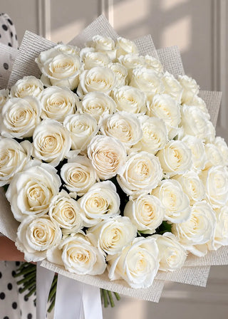 Close view of ivory white roses with cream centers packed into a round dome inside paper wrap