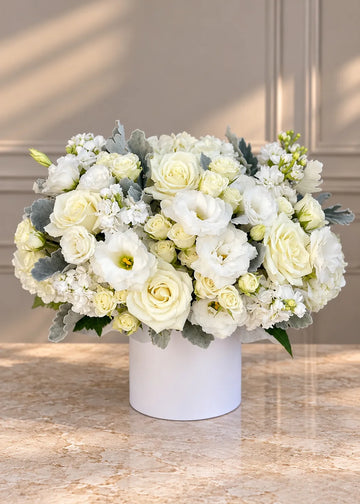 White roses box with white lisianthus, spray roses, stock, hydrangea and dusty miller in a round white box, front view