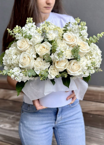 White flower box of white roses, white stock, carnations and hydrangea with eucalyptus, held at waist height