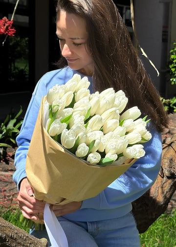 White tulips bouquet in paper wrap with a ribbon, held in both arms outdoors